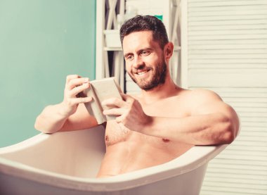 Banyoda seksi adam okuyor. Küvette maço çıplak. Seks ve rahatlama konsepti. adam kaslı bir vücuda sahiptir. Köpükleri suyla dikkatlice yıkayın. kitap sever. banyoda maço zevk kitap. mutlu adam