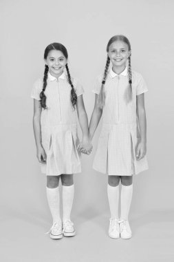 Gümrüklü. Okul üniformalı küçük kızlar. retro bakmak. vintage tarzında çocuklar. eski okul. çocuk modası. sarı arka planda mutlu arkadaşlar. moda güzelliği. çocukluk mutluluğu. kardeşlik kavramı