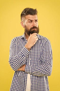 Bazı şüpheler içinde sınat. Düşünceli ifade. Düşünmem gerek. Düşünceli adam karar verme konusunda tereddüt ediyor. Hipster sakallı yüzü bir şeyde emin değil. Sarı arka plan üzerinde düşünceli sakallı adam yakın