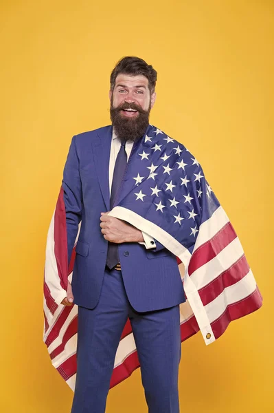 Feliz de ser un buen CEO. Hombre barbudo feliz sonriendo con bandera americana sobre fondo amarillo. Feliz hombre de negocios celebrando el Día de la Independencia. Feliz y orgulloso — Foto de Stock