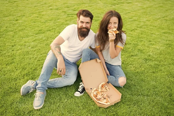 Pizzayı paylaşıyorlar ve yiyorlar. aşk flört çift. aile hafta sonu. fast food. sakallı adam hipster ve sevimli kız pizza yemek. mutlu çift pizza yiyor. yeşil çim üzerinde yaz piknik — Stok fotoğraf