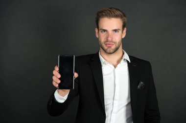 Telefon onu düzenli tutuyor. İş adamı cep telefonunu gösterdi. Cep telefonu olan yakışıklı bir adam. Kişisel ve profesyonel kullanım için telefon. 3G ve 4G. Taşınabilir yaşam tarzı. İrtibatı koparmamak için akıllı telefon