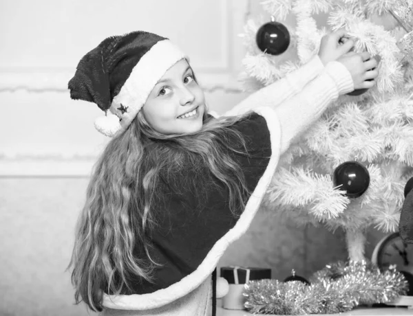 Familientradition. Kind schmückt Weihnachtsbaum mit roten Kugeln Mädchen Kind schmücken Weihnachtsbaum. Geschätzte Urlaubsaktivität. Kind mit Weihnachtsmütze schmückt Weihnachtsbaum — Stockfoto
