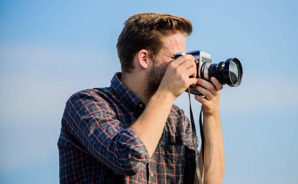 Guy outdoors blue sky background. Handsome blogger guy traveler retro camera. Reporter taking photo. Manual settings. Travel blogger. Vintage equipment. Hipster photographer. Blogger shooting vlog