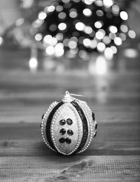 Christmas ornaments concept. Ball ornament on blue wooden surface. Pick colorful decor for christmas tree. Christmas ornament single ball on defocused garland colorful lights background