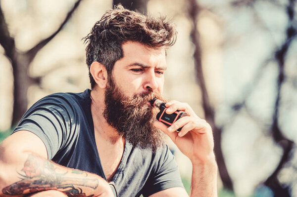 Безопасность и зависимость от здоровья. Вдыхаю пар. Бородатый жестокий мужчина курит электронную сигарету. Хипстерский человек держит ваппинговый прибор. мужчина курит электронную сигарету. Зрелый хипстер с бородой. Мистер... Экспертиза