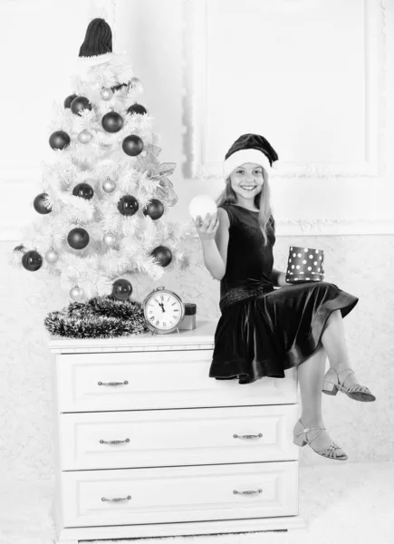 Anak perempuan duduk dekat pohon natal memegang kotak hadiah. Gadis kecil topi Santa bersemangat tentang hadiah Natal atau hadir. Anak-anak merayakan Natal di rumah. Waktunya membuka kado natal. Selamat tahun baru konsep — Stok Foto