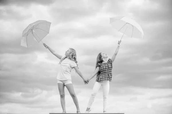 Pronto para qualquer tempo. Vento ou chuvoso estamos preparados. Liberdade e frescura. Previsão meteorológica. Mudança de tempo. Crianças despreocupadas ao ar livre. Meninas amigas com guarda-chuvas céu nublado fundo — Fotografia de Stock