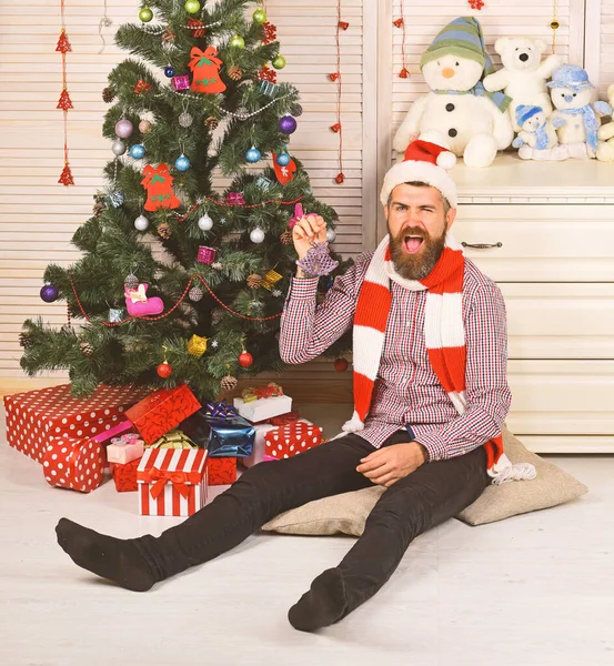 Guy in hat and scarf on floor by Christmas tree — Stock Photo, Image