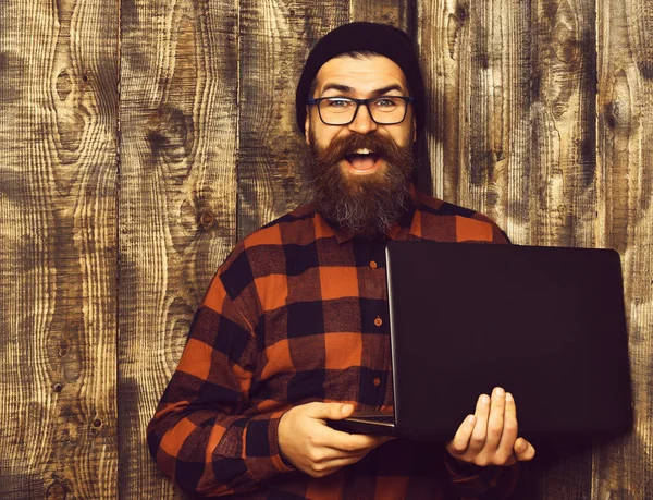 Brodaty brutalny biały hipster trzyma laptop na brązowy vintage drewniane studio tło — Zdjęcie stockowe