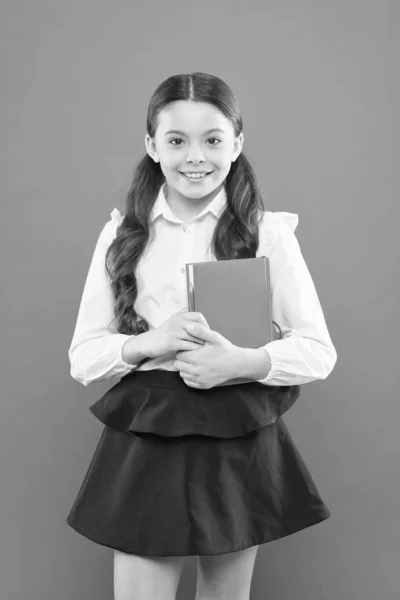 Torniamo a scuola. Questo è il mio libro. scolaretta che scrive appunti su sfondo arancione. piccola ragazza in uniforme scolastica. scheda informativa libro. amante del libro. bambino felice con libro arancione. educazione scolastica moderna — Foto Stock