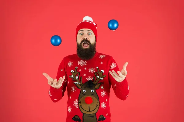 Żonglować piłkami. Zabawa świąteczna. Hipster wesoły brodaty mężczyzna nosić zimowy sweter i kapelusz trzymać kulki czerwone tło. Koncepcja nowego roku. Świąteczne przyjęcie. Zimowy strój. Dekoracje zimowe — Zdjęcie stockowe