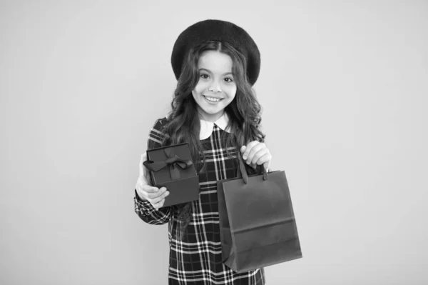 행복한 아이들의 날. 유행 쇼핑 중독자. 아이 패션. 프랑스 베레모에서 행복한 소녀입니다. 노란색 배경에 현재 상자와 아이. 작은 소녀 아이는 쇼핑 백을 개최합니다. 쇼핑 판매. 생일 축하해요 — 스톡 사진