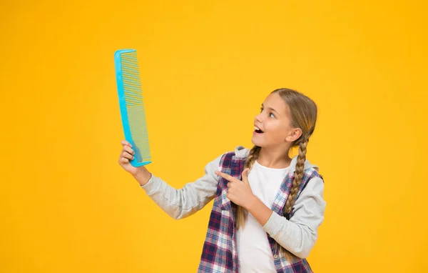 Szkoła fryzjerska. Zajęcia dla fryzjera. Kursy edukacyjne. Zaplątane włosy. Zaopatrzenie fryzjerskie. Dziewczyna trzyma ogromny grzebień. Salon fryzjerski. Grzebieniem włosów. Wesoły dzieciak ze szczotką do włosów — Zdjęcie stockowe