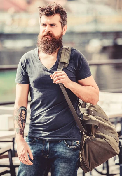 Travelling and vacations concept. Muscular man with beard and mustache carrying big sporty bag. Tourist explore city with luggage. Heavy bag on his shoulder. Carry things in big bag on shoulder