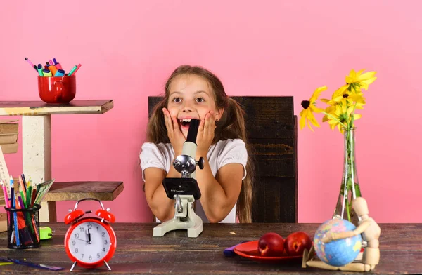 Colegiala en el escritorio con flores amarillas, reloj rojo, fruta, globo — Foto de Stock