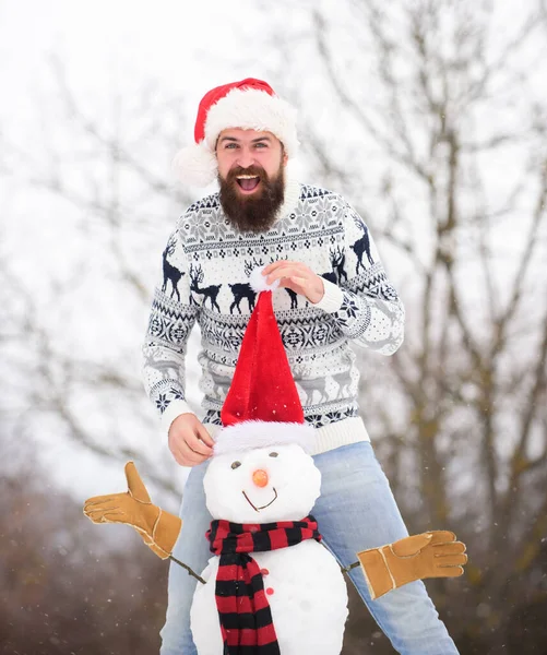 休息だ。冬の活動。クリスマスだ。サンタの帽子は雪で遊ぶ。冬休みの屋外。寒い日の暖かいセーター。髭の男が雪だるまを作る。ハッピーヒップスターxmasを祝う準備ができて — ストック写真