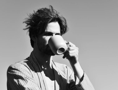 Mavi çizgili pijamalı, elinde fincanla beyaz maço.