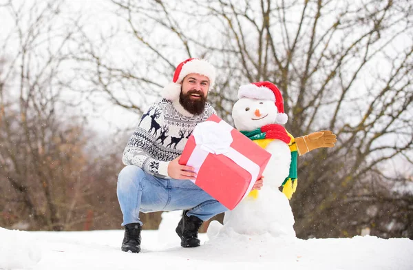 Бородатий чоловік будує сніговика. З Новим роком. Санта людина дарує подарунок на відкритому повітрі. зимовий відпочинок. теплий светр в холодну погоду. щасливий хіпстер готовий до Різдва. активність в зимовий сезон. Веселого Різдва — стокове фото
