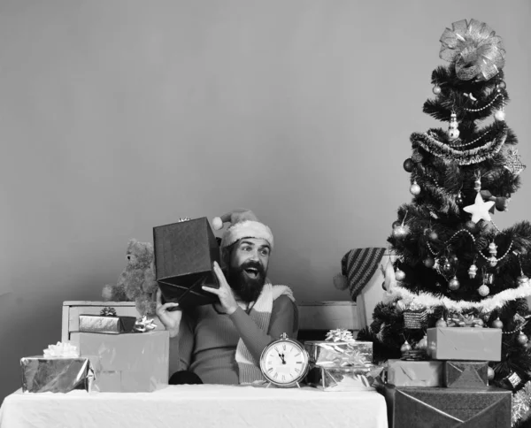 Санта Клаус відкриває подарунки біля прикрашеного дерева на червоному тлі. — стокове фото