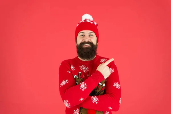 Volwassen rendier met baard trui. brutale hipster in gebreide muts rode achtergrond. draag kerststemming. mannelijke breimode. Grappig uitziende man die wijst. nog steeds geloven in de kerstman — Stockfoto