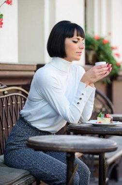 Çekici, zarif, esmer bir kadın tatlı ve kahve kafesi terası arka planının tadını çıkarıyor. Keyifli zaman ve rahatlama. Lezzetli ve gurme atıştırmalıkları. Kahve ve tatlı ile kafeyi rahatlatan bir kız. Tatlı konsepti