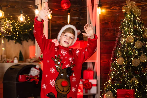 hello santa. little boy in red reindeer sweater. kid in santa claus hat have fun at home. merry christmas everyone. wants xmas present. best winter holidays. happy teenager celebrate new year party