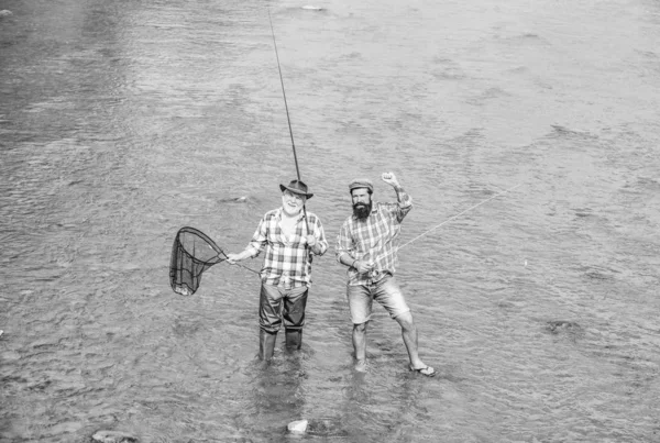 Летние выходные. Рыбачить вместе. Мужчины стоят в воде. Отличная идея. Команда рыбаков. Счастливого рыбака с удочкой и сетью. Хобби и спортивные мероприятия. Мужская дружба. Отец и сын рыбачат — стоковое фото