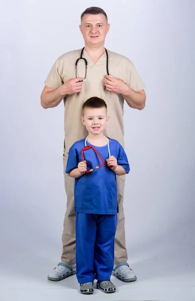 Profesión futura. Quiero ser médico como papá. Lindo niño jugar juego médico. Doctor de familia. Concepto de pediatra. Padre doctor con estetoscopio e hijo pequeño médico uniforme. Medicina y asistencia sanitaria — Foto de Stock