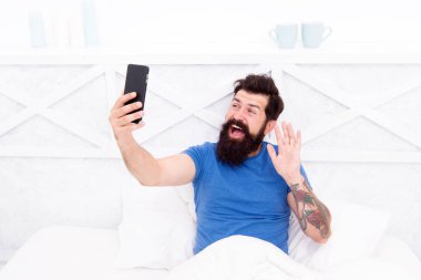 Merhabalar. Sakallı adam yatakta akıllı telefon kullanır. Mobil teknoloji. Taşınabilir yaşam tarzı için yeni bir teknoloji. Modern hayat. Evdeki kablosuz iletişim teknolojisi. Mobil teknolojiden yararlan.