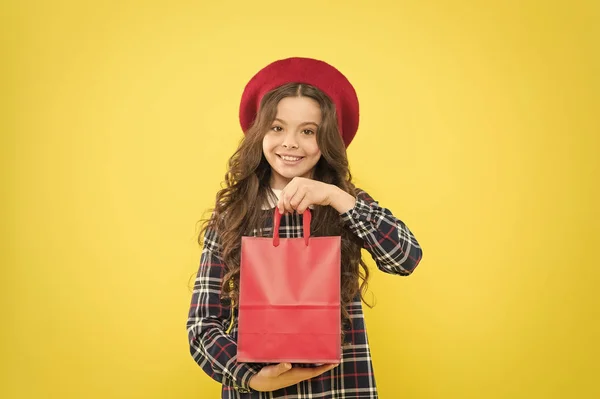 Bolsa fácil de usar. Chica feliz sosteniendo bolsa de compras sobre fondo amarillo. Niño sonriendo con bolsa de papel después de la venta de moda. Niño pequeño que lleva la compra en rojo no bolsa de transporte de comestibles —  Fotos de Stock