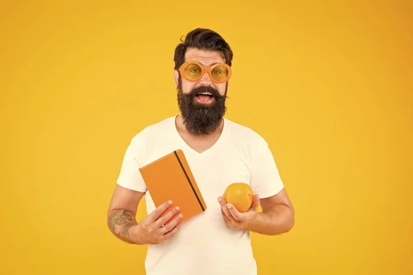 Essere orgogliosi di essere geek in te. Che secchione. Uomo barbuto in occhiali geek tenendo arancione e libro su sfondo giallo. Hipster in stile geek chic scegliere cibo sano per il cervello — Foto Stock