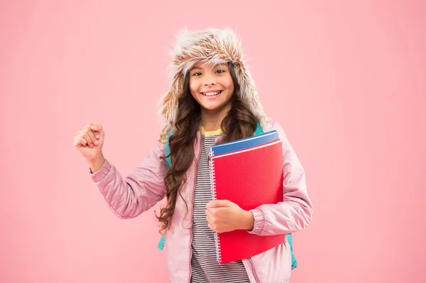 Ta mig när jag är som bäst. skolflicka bär ryggsäck och böcker går hem. Inga fler prov. liten glad flicka öronlapp hatt. Tillbaka till skolan. vintersemester. unge varma kläder rosa bakgrund. elev i vardagen — Stockfoto