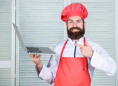 Aşçılık okulu. Şapkalı ve önlüklü hippi internetten ürün alıyor. İnternetten alışveriş. Teslimat servisi. Aşçı adam internette yemek pişiriyor. Market çevrimiçi. Mutfakta şef dizüstü bilgisayar.