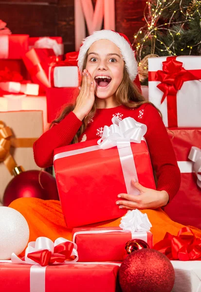 Een kind met een kerstmuts met veel geschenkdozen. succesvol winkelen op de kerstmarkt. versierd met geschenken. kerstpakketten te koop. Vrolijke kerstman helper soort cadeautjes. glimlachende winkelassistent — Stockfoto