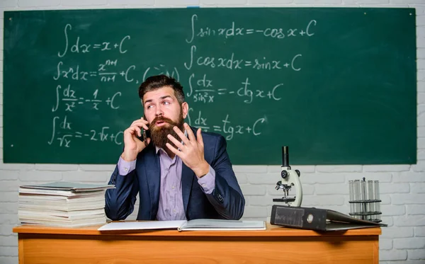 Calling parents. Call colleague ask advice. Teacher bearded man talk mobile phone. Pedagogue keep in touch with colleagues. School teacher call mobile phone while sit classroom chalkboard background