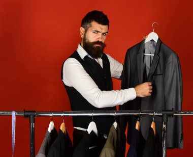 Asistan ya da satıcı elbise askılarının yanında gri takım elbise tutuyor..