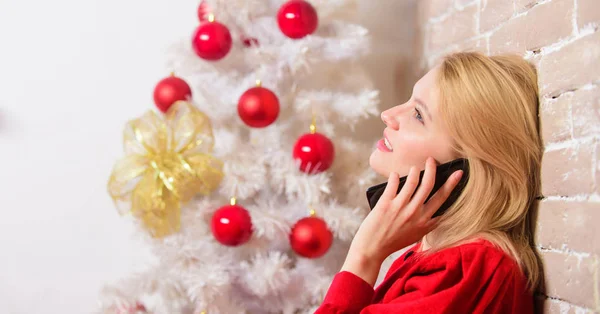Wishing everyone merry christmas. Christmas wishes concept. Woman pretty peaceful dreamy face hold smartphone enjoy mobile phone conversation. Girl near christmas tree close up. Waiting for christmas