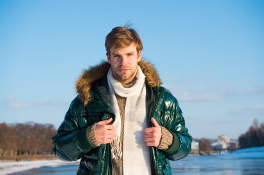 Fotoğraf için poz veriyorum. Yakışıklı, yeşil kabarık ceketli adam. Adam güneşli kış gününün tadını çıkarıyor. Erkek sezonluk moda. Soğuk algınlığı ve grip Kürk kapüşonlu erkek. Sıcak ve rahat hissediyorum. favori sezon