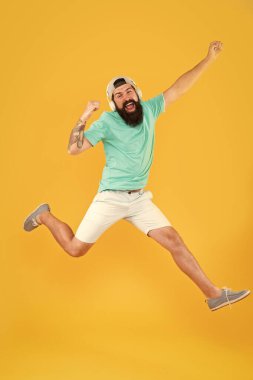 Mutluluk şarkısı. Sakallı adam sarı arka planda mutlulukla atlıyor. Mutlu hipster modern kulaklıklar müzik dinleme keyfini çıkarın. Mutluluk frekansı. Mutluluk ve olumlu düşünme için müzik