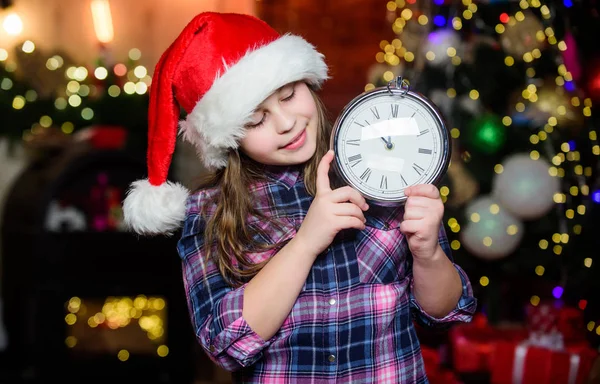 Christmas is here. Time to celebrate. Happy new year. Elf child with clock. Xmas tree. Happy holiday. Little girl in red hat. Happy christmas. Santa claus little girl. Christmas time