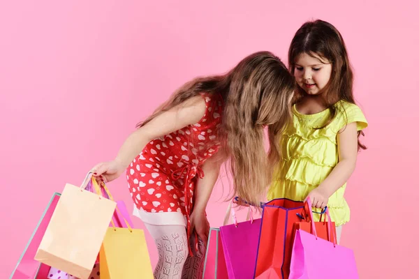 Dziewczyny z zainteresowanymi twarzami trzymają pakiety izolowane na różowo — Zdjęcie stockowe