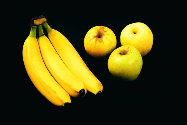 Muz yanındaki siyah arka plan üzerine üç elma — Stok fotoğraf