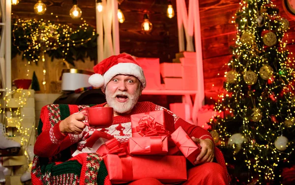 Доставка подарков. Зимние каникулы. Пожилой дедушка дома. Концепция традиций. Санта Клаус возле рождественской елки. Счастливого Рождества. Старший бородатый Санта Клаус. Санта-Клаус расслабляется в кресле — стоковое фото