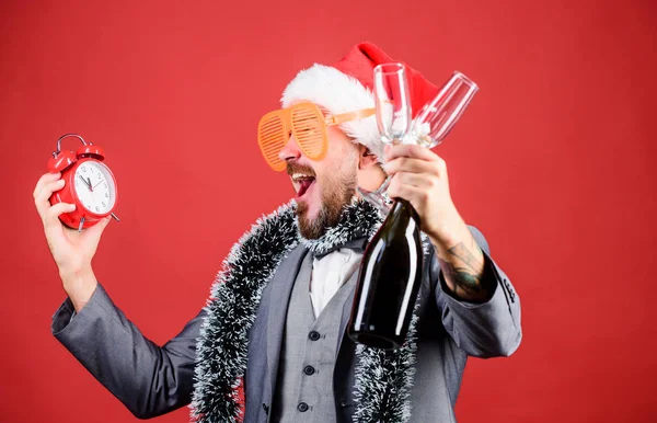 dont be late. happy new year. businessman santa hat with tinsel and clock. christmas is fun time. man business drink champagne from glasses. time for winter holidays. man celebrating xmas party