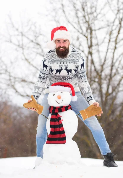 Winter holidays. happy hipster ready for xmas. winter season activity. its christmas. winter holiday outdoor. warm sweater in cold weather. man santa hat play with snow. bearded man build snowman — Stock Photo, Image