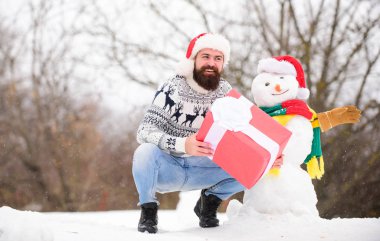 Noel tatili. Adam dışarıda hediye veriyor. Mutlu hipster Noel 'e hazır. Sakallı adam kardan adam yapar. Mutlu yıllar. Kış tatili Soğuk havada sıcak kazak. Kış mevsimi. Mutlu Noeller.