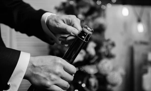 Lets celebrate. Open champagne and celebrate holiday. Celebrate new year with champagne drink. Toast and cheers concept. Male hands opening champagne bottle on christmas decorations background