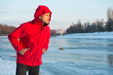 Soğuk iklim için sıcak kıyafetler. Hava tahmini. İnsan ve doğa. Adam gün batımında karlı arazide yürüyor. seyahat ve keşif. Kırmızı parkalı adam. Kış erkek modası. kopyalama alanı. Güzel bir kış tatili