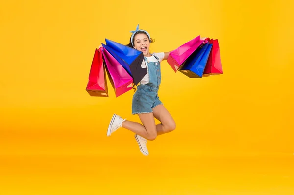 Pośpiesz się. Kupuj szybciej. Szczęśliwa dziewczyna skacze z torbami na zakupy. Małe dziecko uśmiecha się papierowymi torbami. Przygotowania do świąt i uroczystości. Zakupy w czarny piątek. Inspirujące zakupy. Udane porozumienie — Zdjęcie stockowe